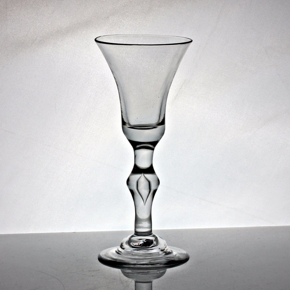 An 18th-century clear glass wine glass featuring a flared bell-shaped bowl, a turned baluster stem with knops, and a wide domed foot.
