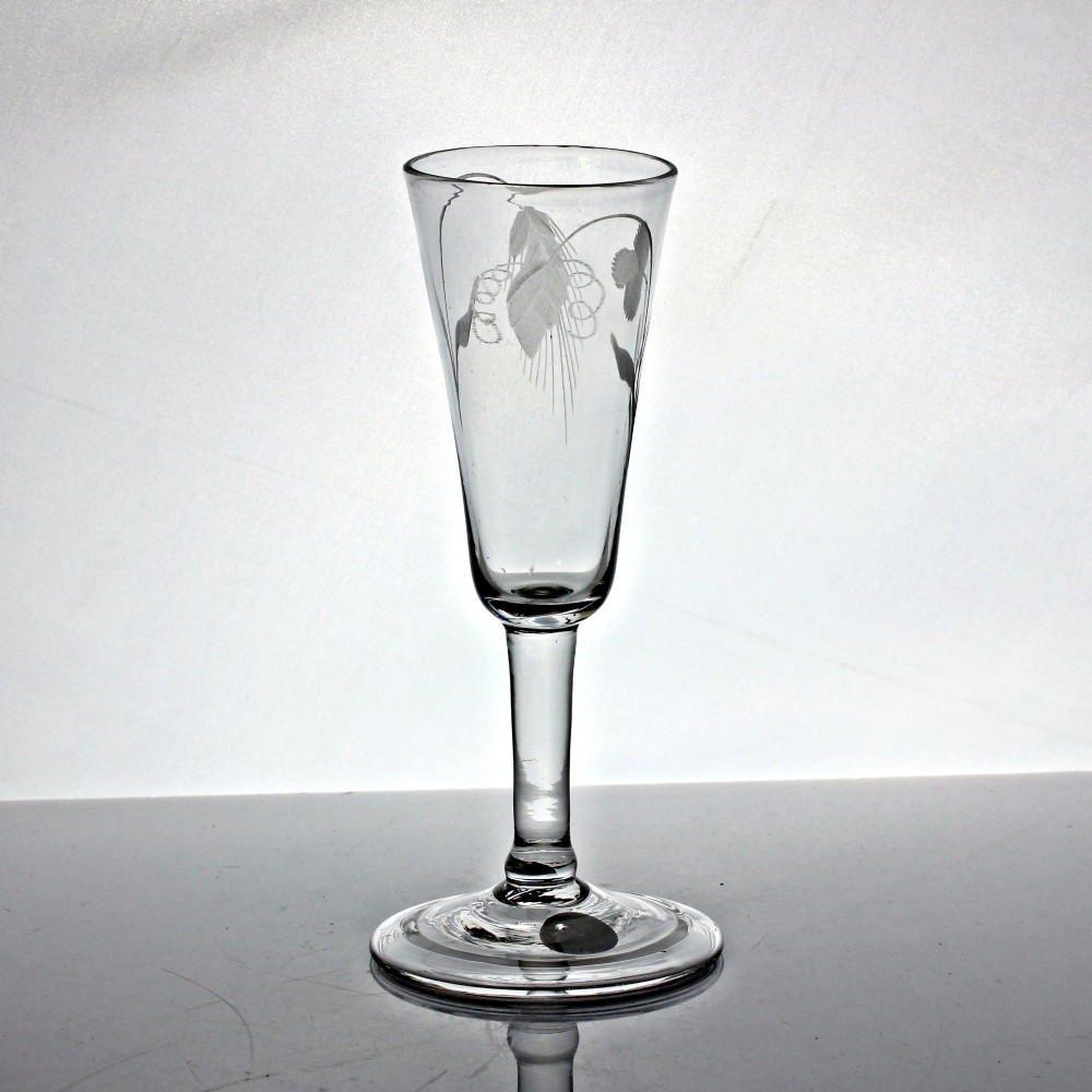 An antique clear glass ale flute featuring wheel-engraved hop and barley motifs on a tall bowl supported by a balustroid stem and folded foot.