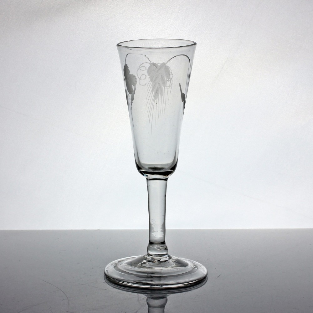 An antique clear glass ale flute featuring wheel-engraved hop and barley motifs on a tall bowl supported by a balustroid stem and folded foot. View II