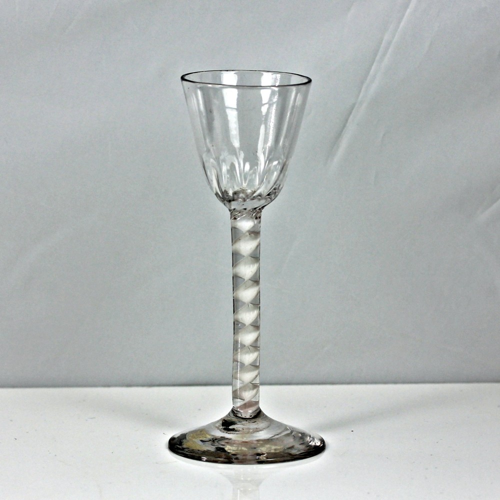 An 18th-century Georgian clear glass wine glass featuring a single series opaque twist stem, a rounded funnel bowl with fluted base, and a conical foot.