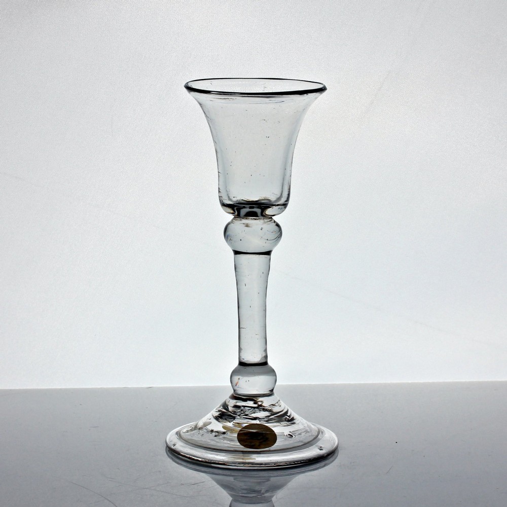 A clear hand-blown Georgian drinking glass featuring a flared bell bowl, a balustroid stem with knops, and a folded conical foot.