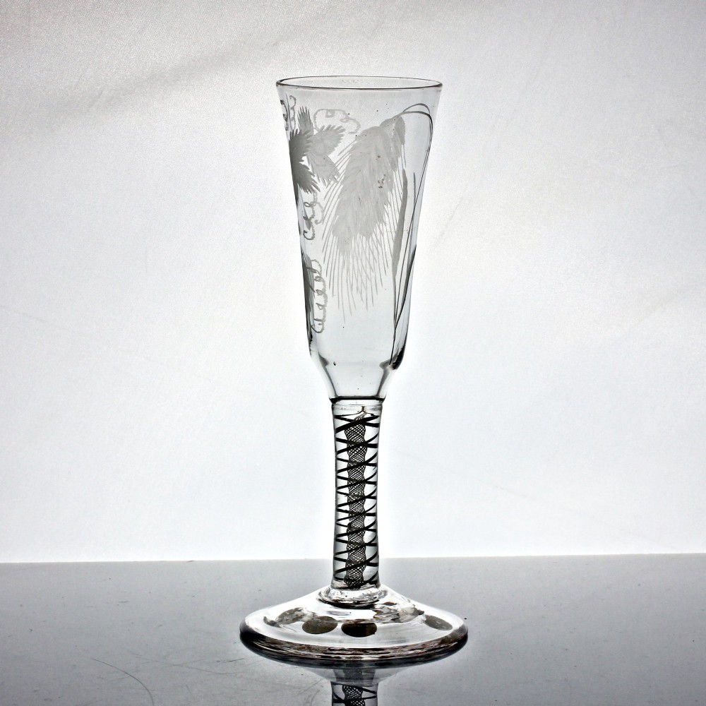 An antique clear glass ale flute featuring a double series opaque twist stem and an engraved hop and barley motif on the bowl. View III