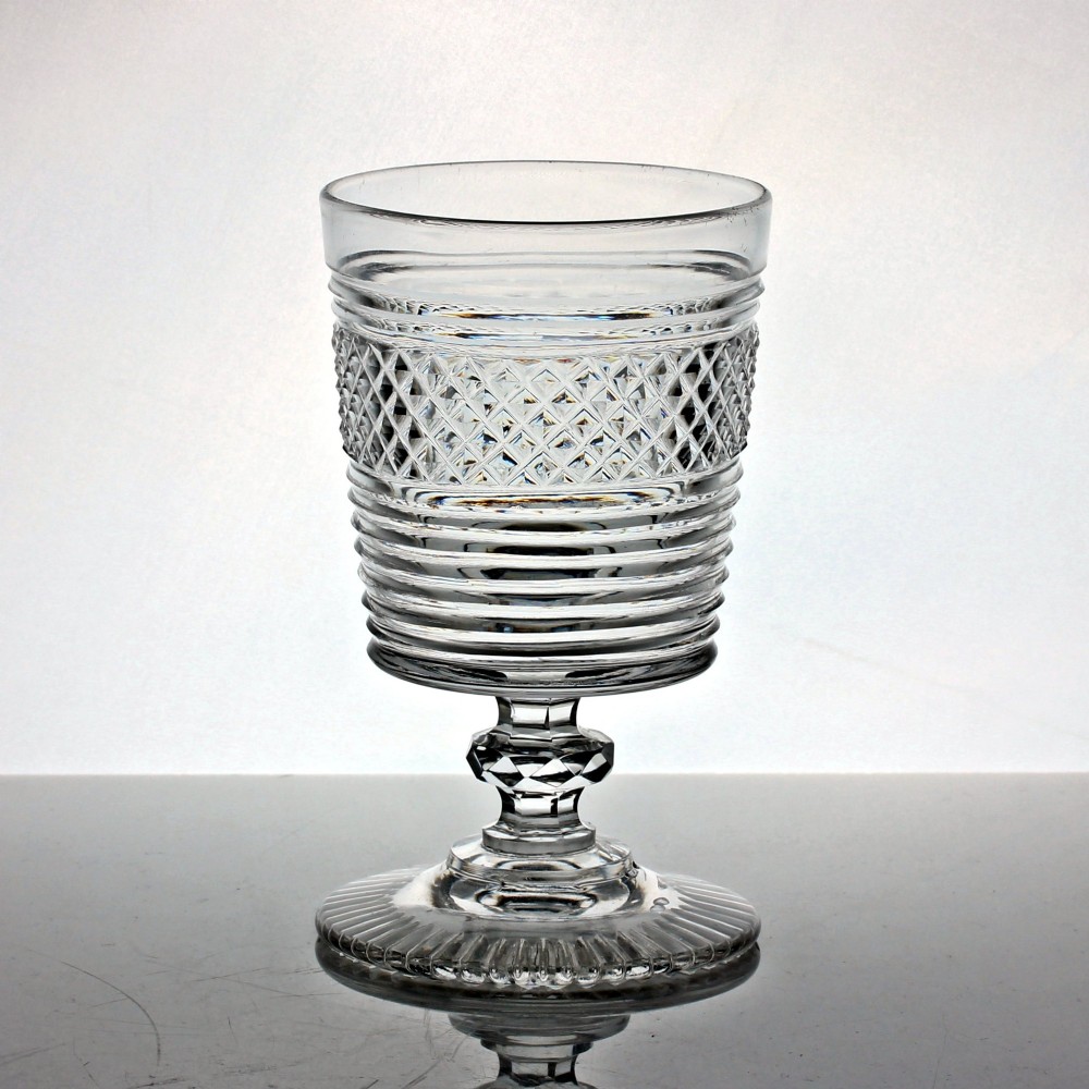 A clear cut glass rummer with a bucket-shaped bowl decorated with diamond cuts and horizontal rings, resting on a faceted stem knop and a circular cut foot.