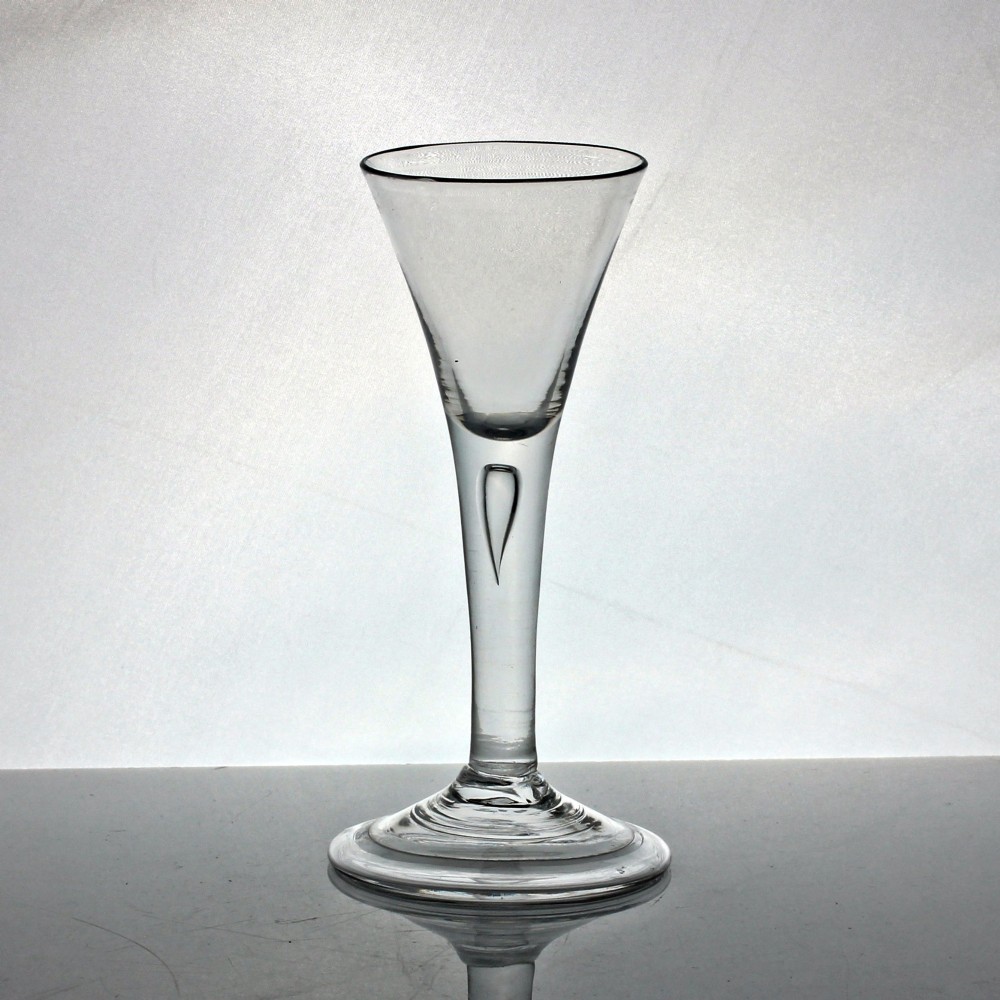 An 18th-century clear glass wine glass with a funnel-shaped bowl, a plain stem featuring an air tear drop inclusion, and a wide folded foot.