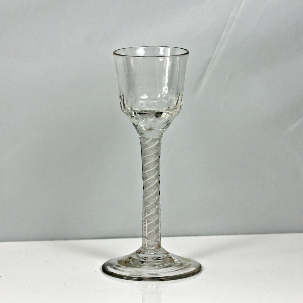 A clear Georgian wine glass featuring a wrythen moulded bowl resting on a stem with an internal double series opaque twist pattern and a broad conical foot.