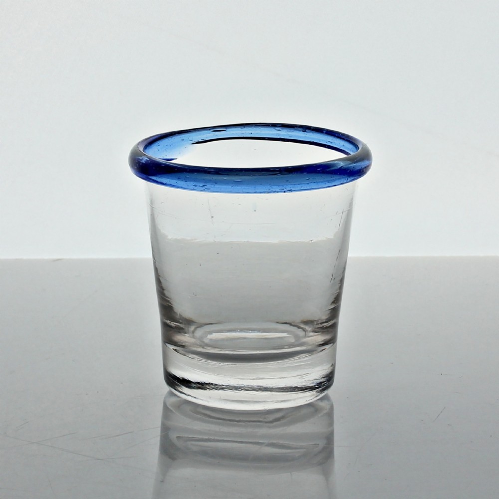 A small clear hand-blown glass tumbler featuring an applied cobalt blue glass rim around the top opening.