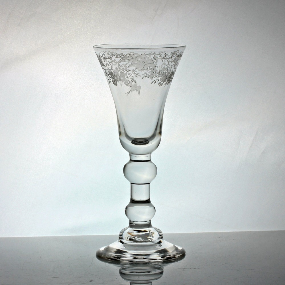 A clear Georgian lead glass goblet featuring a bell-shaped bowl with wheel-engraved floral and bird motifs, supported by a heavy baluster stem on a domed foot.