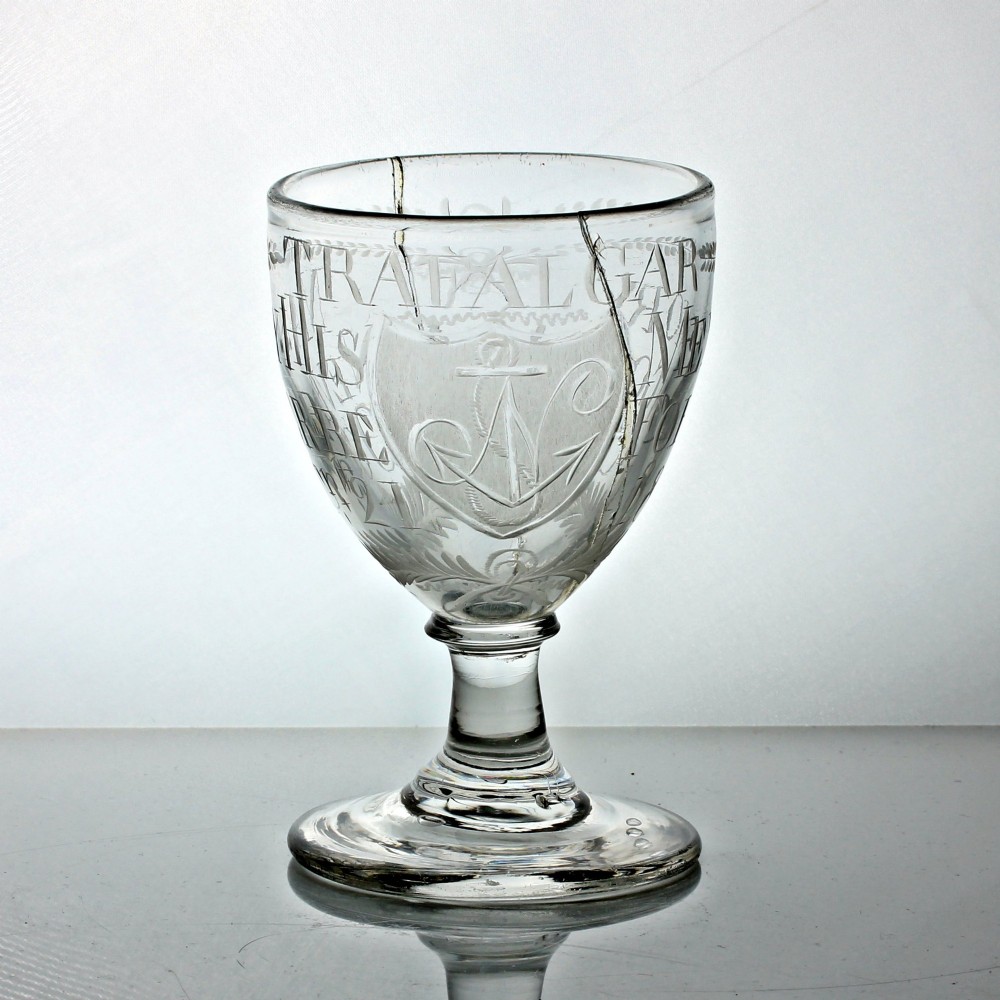 An antique clear glass rummer featuring hand-engraved naval motifs, text referencing Trafalgar, a short stem, and a circular foot.