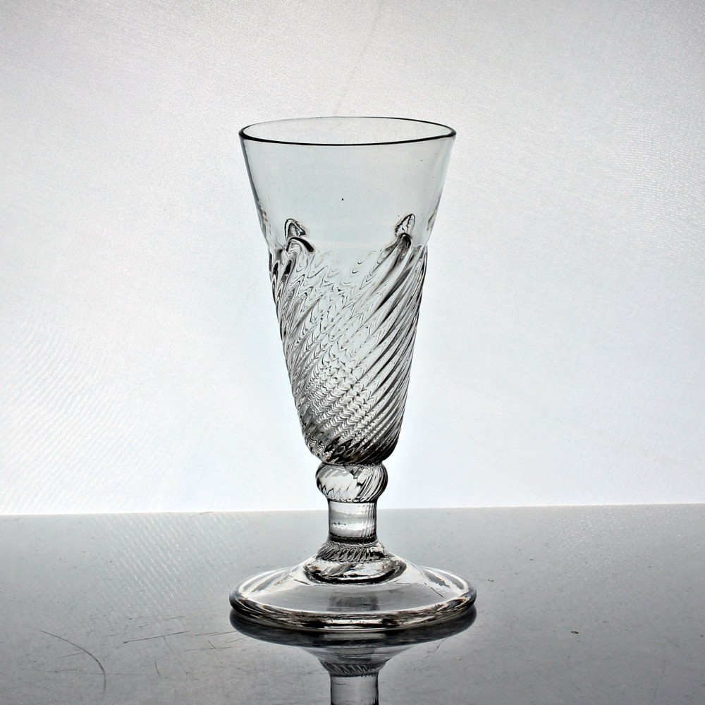 A clear Georgian hand-blown dwarf ale glass featuring a funnel-shaped bowl with diagonal flammiform moulding on a short knopped stem and conical foot.