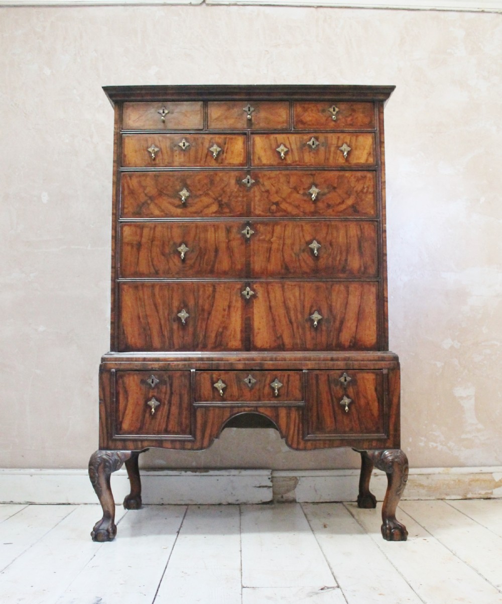 An 18th-century walnut chest on stand featuring figured veneers, brass drop handles, a shaped apron, and cabriole legs with carved knees.