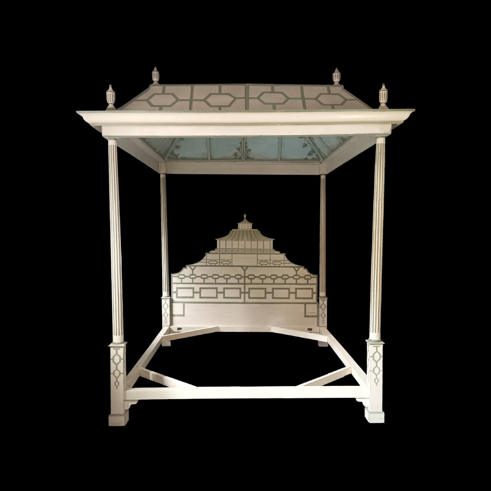 A cream-painted Edwardian four-poster bed frame featuring a pagoda-shaped headboard, decorative geometric fretwork, urn finials, and a painted canopy underside.