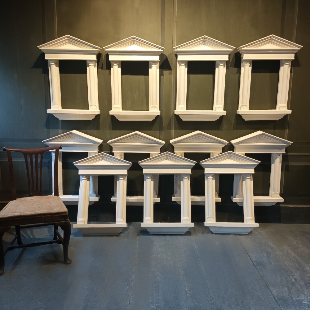 A white plaster tabernacle picture frame featuring a triangular pediment supported by two smooth classical columns resting on a projecting plinth base. View III