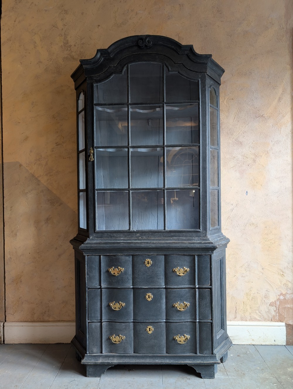 A tall dark grey painted Dutch vitrine cabinet featuring a shaped top hood, glazed upper doors, and three lower drawers with brass handles. View II
