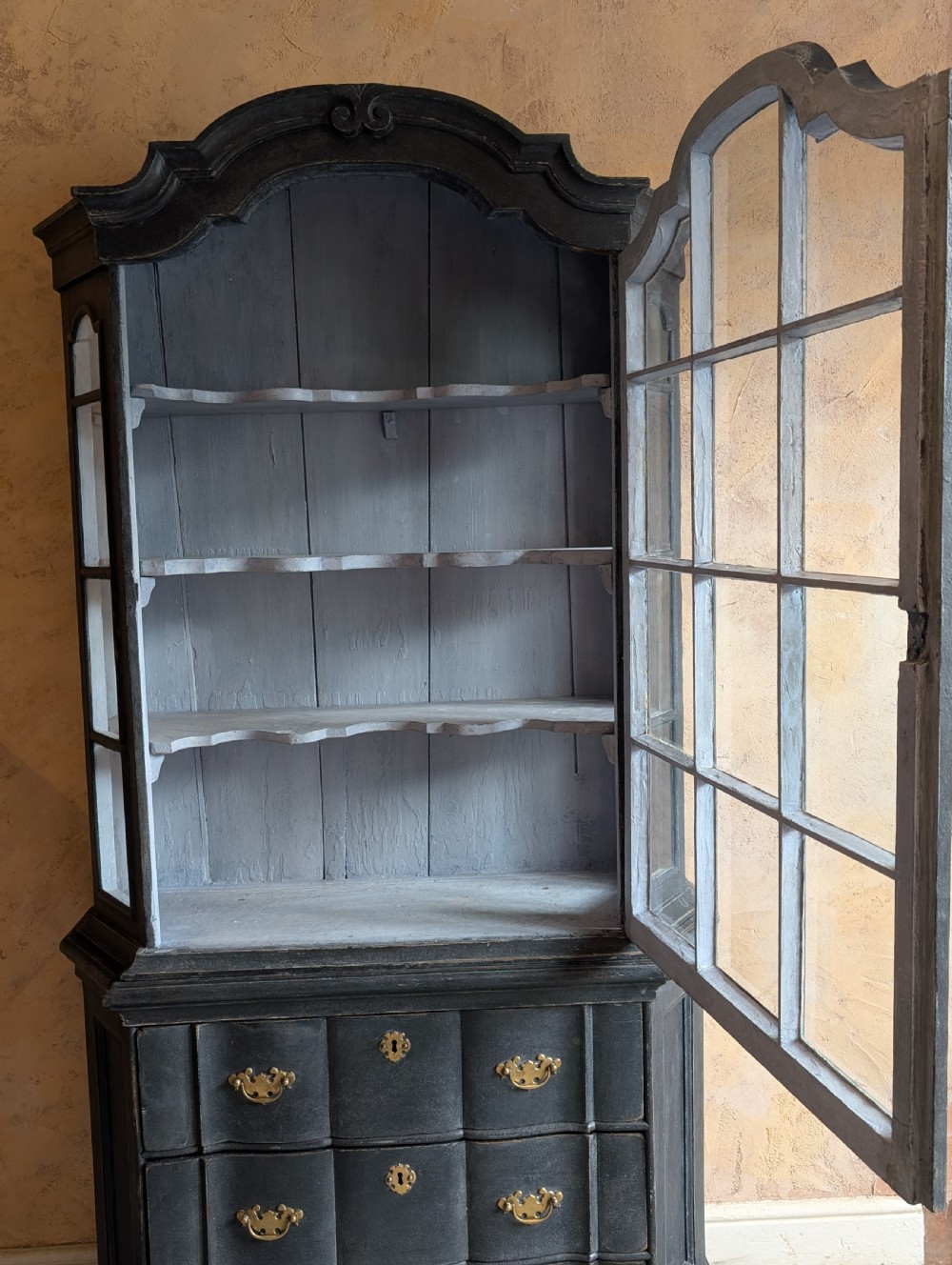 A tall dark grey painted Dutch vitrine cabinet featuring a shaped top hood, glazed upper doors, and three lower drawers with brass handles. View IV