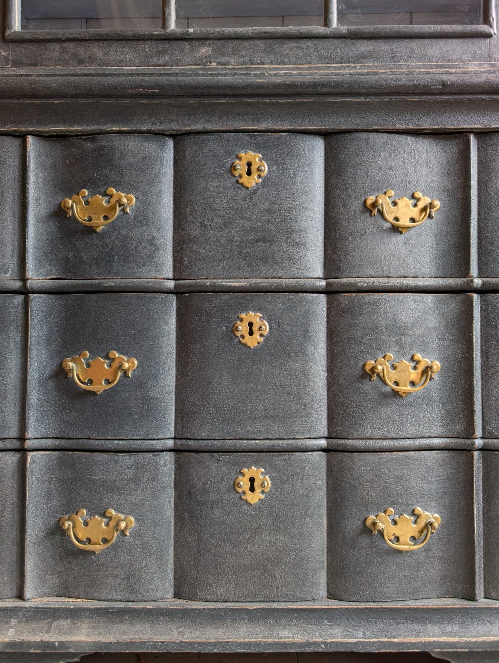 A tall dark grey painted Dutch vitrine cabinet featuring a shaped top hood, glazed upper doors, and three lower drawers with brass handles. View VI