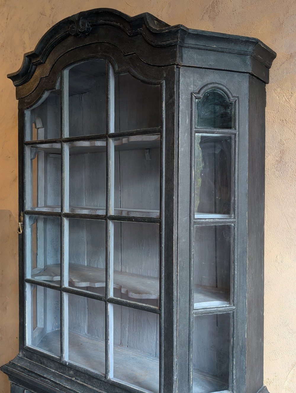 A tall dark grey painted Dutch vitrine cabinet featuring a shaped top hood, glazed upper doors, and three lower drawers with brass handles. View VIII