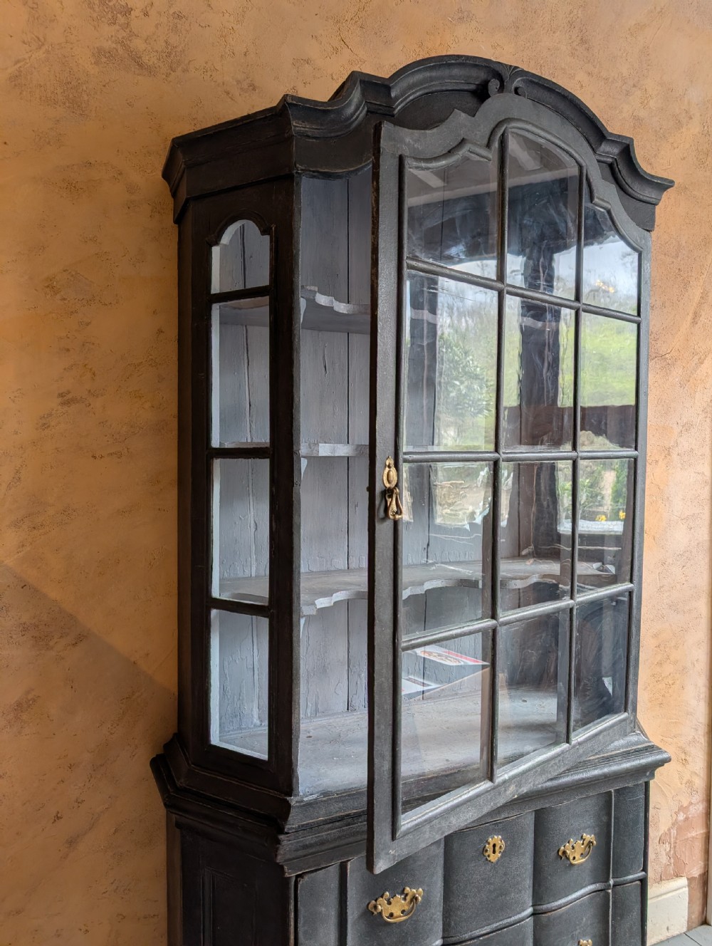 A tall dark grey painted Dutch vitrine cabinet featuring a shaped top hood, glazed upper doors, and three lower drawers with brass handles. View XI