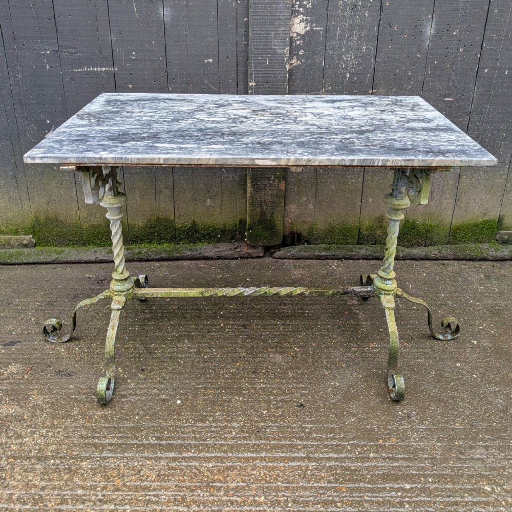 A rectangular grey veined marble top resting on a weathered cast iron base with twisted legs and scroll feet.