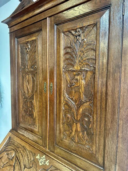fig 1. A Victorian carved oak bureau bookcase featuring a scrolled pediment top, two carved upper doors, a slope-front writing surface with relief carvings, and four lower drawers with brass handles.