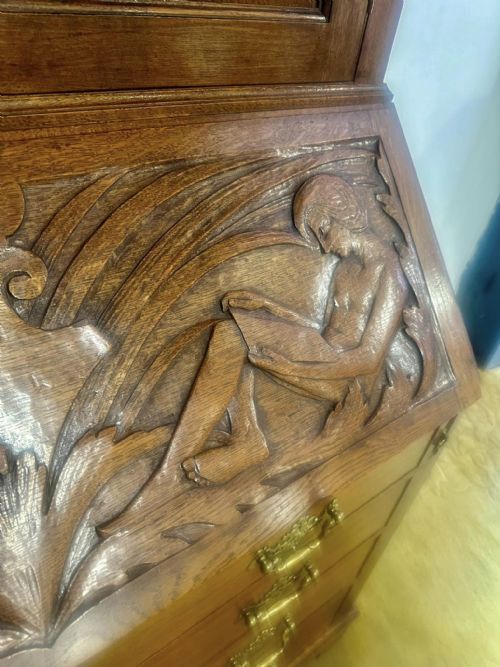 fig 2. A Victorian carved oak bureau bookcase featuring a scrolled pediment top, two carved upper doors, a slope-front writing surface with relief carvings, and four lower drawers with brass handles.