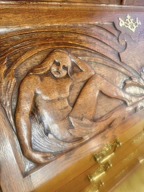 fig 3. A Victorian carved oak bureau bookcase featuring a scrolled pediment top, two carved upper doors, a slope-front writing surface with relief carvings, and four lower drawers with brass handles.