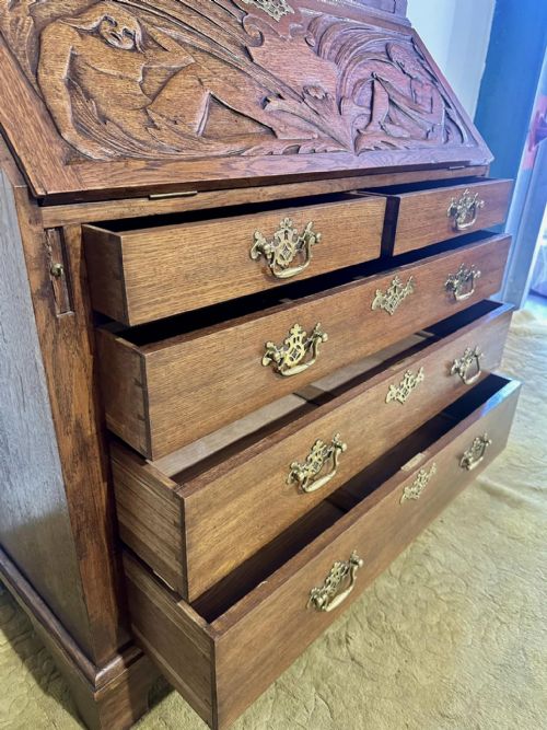 fig 4. A Victorian carved oak bureau bookcase featuring a scrolled pediment top, two carved upper doors, a slope-front writing surface with relief carvings, and four lower drawers with brass handles.