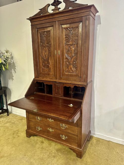 fig 8. A Victorian carved oak bureau bookcase featuring a scrolled pediment top, two carved upper doors, a slope-front writing surface with relief carvings, and four lower drawers with brass handles.