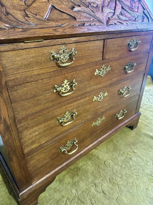 fig 9. A Victorian carved oak bureau bookcase featuring a scrolled pediment top, two carved upper doors, a slope-front writing surface with relief carvings, and four lower drawers with brass handles.