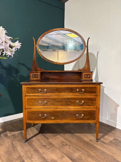 fig 3. An Edwardian mahogany dressing table with an oval swivelling mirror, two upper trinket drawers, three main drawers with satinwood inlay borders, and tapered legs on castors.