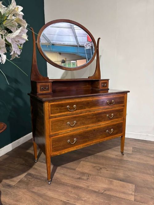 fig 5. An Edwardian mahogany dressing table with an oval swivelling mirror, two upper trinket drawers, three main drawers with satinwood inlay borders, and tapered legs on castors.