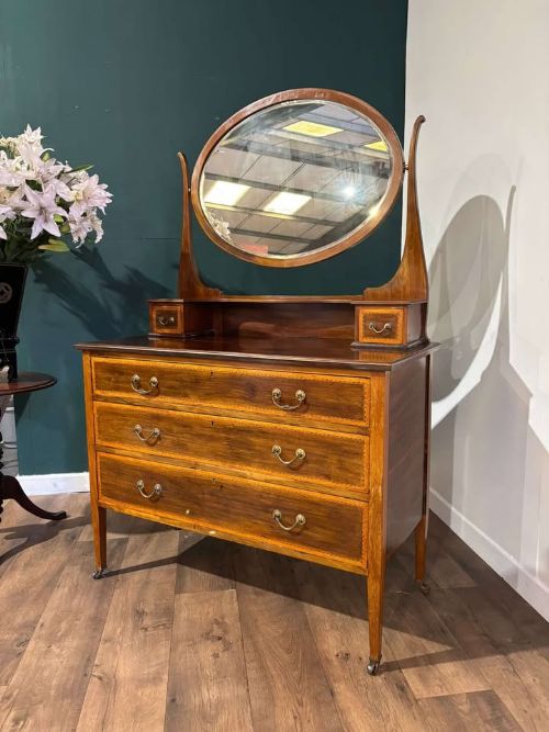 fig 7. An Edwardian mahogany dressing table with an oval swivelling mirror, two upper trinket drawers, three main drawers with satinwood inlay borders, and tapered legs on castors.