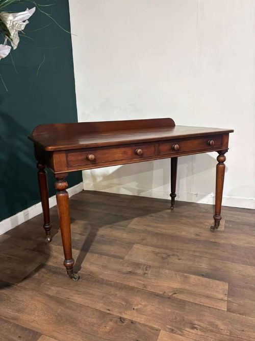 fig 2. A Victorian mahogany washstand featuring two drawers with wooden knob handles, a low gallery back, turned legs, and brass castors.