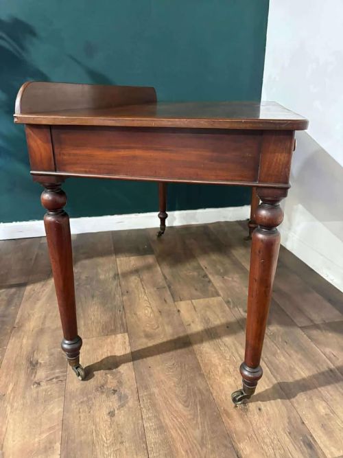 fig 5. A Victorian mahogany washstand featuring two drawers with wooden knob handles, a low gallery back, turned legs, and brass castors.