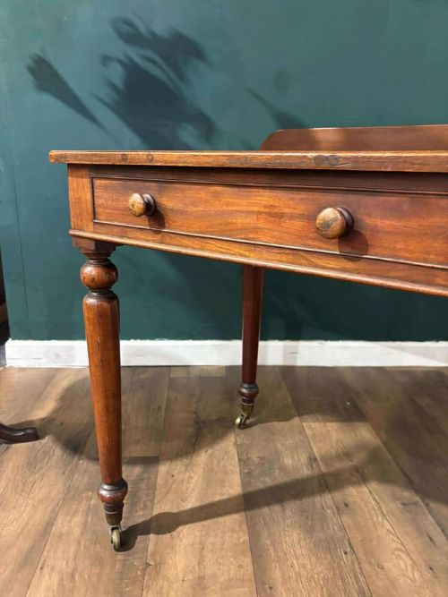 fig 7. A Victorian mahogany washstand featuring two drawers with wooden knob handles, a low gallery back, turned legs, and brass castors.