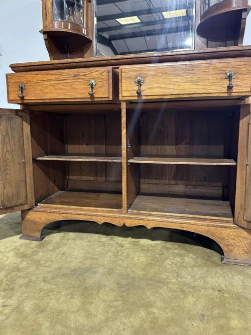 fig 2. A golden oak sideboard featuring a central mirror back flanked by two curved leaded glass cabinets above two drawers and two cupboard doors.