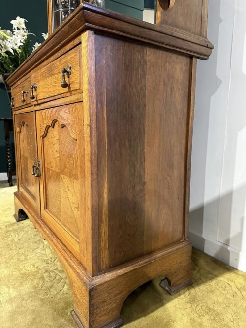 fig 3. A golden oak sideboard featuring a central mirror back flanked by two curved leaded glass cabinets above two drawers and two cupboard doors.