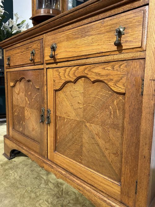fig 4. A golden oak sideboard featuring a central mirror back flanked by two curved leaded glass cabinets above two drawers and two cupboard doors.