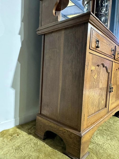 fig 5. A golden oak sideboard featuring a central mirror back flanked by two curved leaded glass cabinets above two drawers and two cupboard doors.