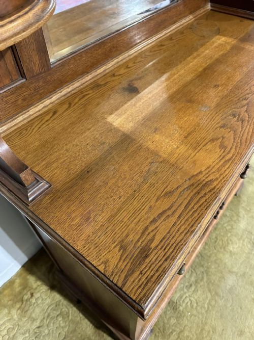 fig 7. A golden oak sideboard featuring a central mirror back flanked by two curved leaded glass cabinets above two drawers and two cupboard doors.