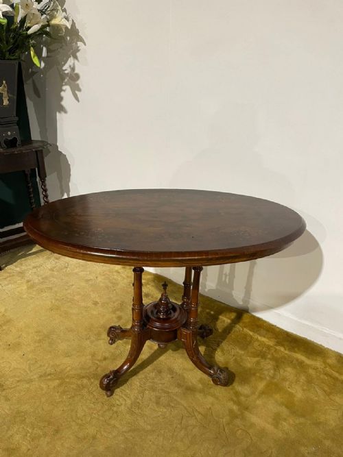 fig 2. Victorian oval burr walnut occasional table featuring four turned column supports, a central finial, and carved legs on castors.