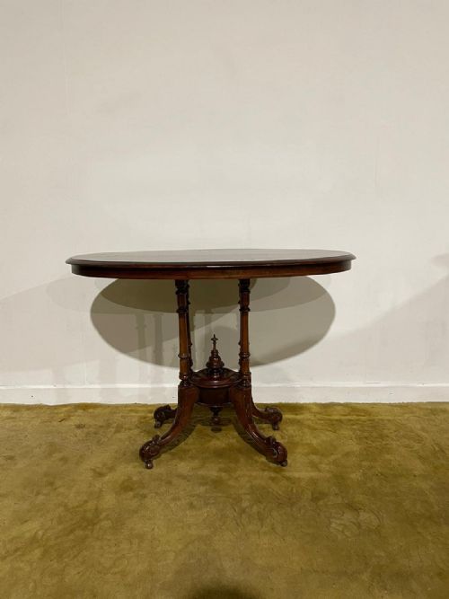 fig 3. Victorian oval burr walnut occasional table featuring four turned column supports, a central finial, and carved legs on castors.