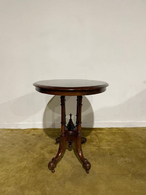 fig 4. Victorian oval burr walnut occasional table featuring four turned column supports, a central finial, and carved legs on castors.