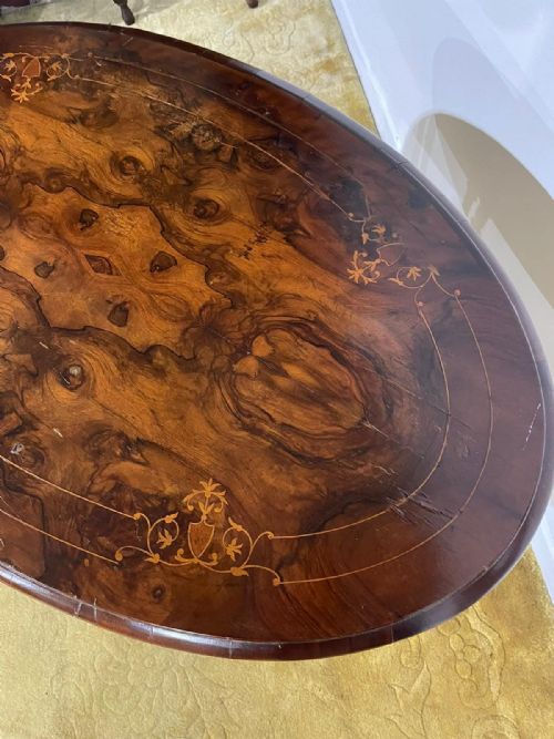 fig 6. Victorian oval burr walnut occasional table featuring four turned column supports, a central finial, and carved legs on castors.