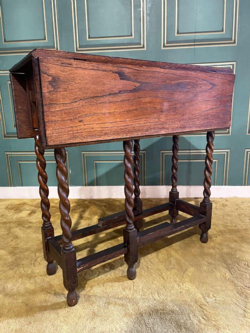 fig 1. A dark brown oak drop-leaf table with folded side flaps standing on six barley twist legs connected by lower stretchers.
