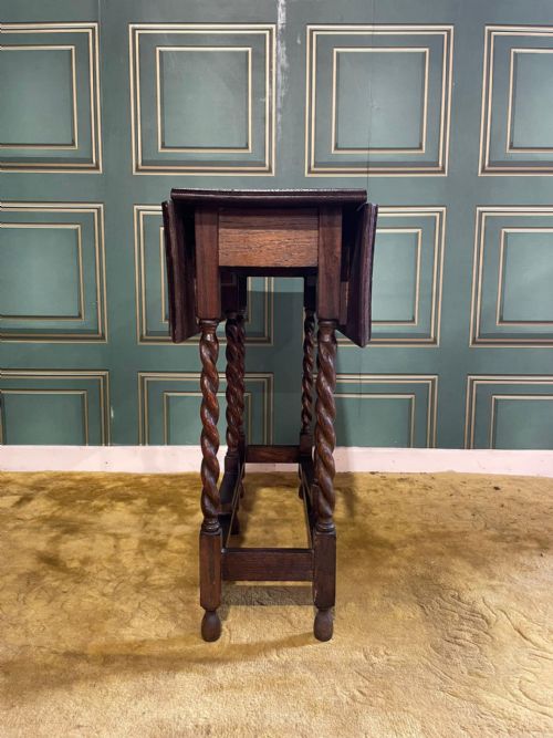fig 2. A dark brown oak drop-leaf table with folded side flaps standing on six barley twist legs connected by lower stretchers.