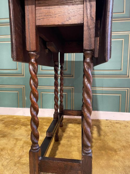 fig 3. A dark brown oak drop-leaf table with folded side flaps standing on six barley twist legs connected by lower stretchers.