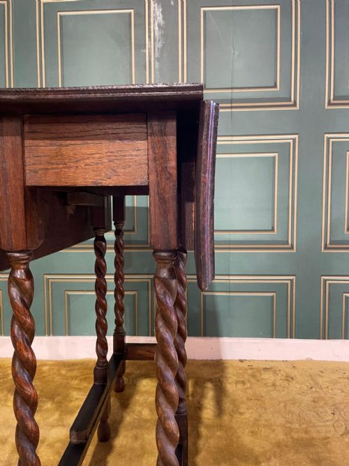 fig 4. A dark brown oak drop-leaf table with folded side flaps standing on six barley twist legs connected by lower stretchers.