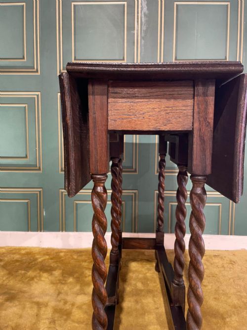 fig 6. A dark brown oak drop-leaf table with folded side flaps standing on six barley twist legs connected by lower stretchers.
