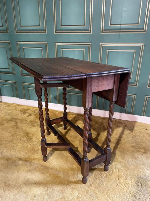 fig 7. A dark brown oak drop-leaf table with folded side flaps standing on six barley twist legs connected by lower stretchers.