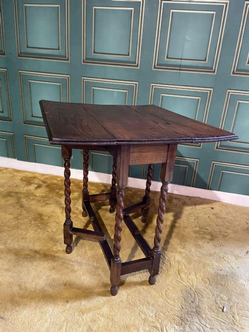 fig 8. A dark brown oak drop-leaf table with folded side flaps standing on six barley twist legs connected by lower stretchers.